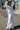 A woman standing outside at the beach wearing white full leg trousers with a matching shirt jacket.