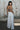 A woman standing outside by a mural wearing white full leg trousers with a tapestry bra top, back view.