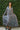Woman wearing a long gray dress against a green leafy background