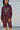 A woman wearing a long-sleeve burgundy jumpsuit with a tie waist standing in front of a white garage door.