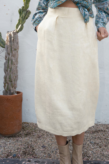 Person wearing a cream skirt with a cactus plant in the background