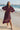 Woman in a burgundy dress standing on a beach with ocean and pier in the background