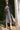 Woman in a gray dress and cardigan standing next to a palm tree