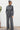 Woman wearing a gray jumpsuit standing against a white wall.