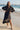 Woman in a black dress standing on a beach with a pier in the background