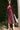 Woman in a burgundy dress standing outdoors with greenery in the background