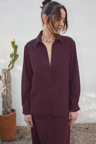 Woman wearing a balck fig outfit standing next to a potted plant against a textured wall.