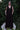 Woman in a black dress standing on a white bench with greenery in the background