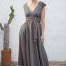 Woman wearing a sleeveless dress with a belt, standing against a white wall with a cactus plant.