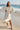 Woman in an alabaster dress standing on a beach with a pier in the background