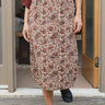 Person wearing a patterned skirt and maroon top standing on a wooden deck.