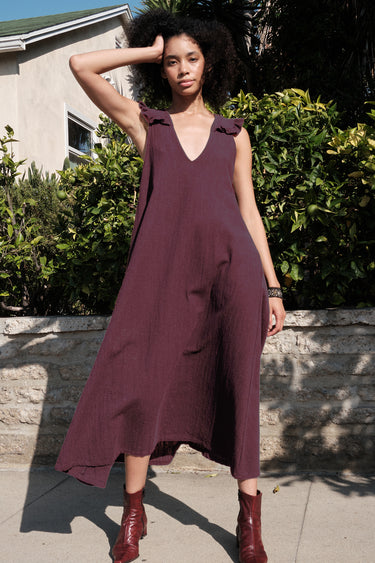 Woman wearing a burgundy dress standing outdoors with greenery and a building in the background
