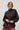 Person wearing a jet black blouse and red pants against a white background