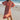 Woman in a persimmon dress standing on a beach with a pier in the background