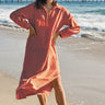 Woman in a persimmon dress standing on a beach with a pier in the background