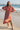 Woman in a persimmon dress standing on a beach with a pier in the background