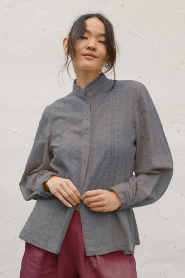 Woman wearing a gray blouse with intricate detailing against a white background