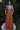 Woman wearing a persimmon dress sitting on a white bench with greenery in the background