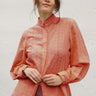 Woman wearing persimmon blouse with lace details against a white background
