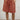 Person wearing persimmon shorts and beige boots against a white wall.