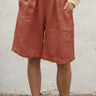Person wearing persimmon shorts and beige boots against a white wall.