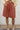 Person wearing persimmon shorts and beige boots against a white wall.