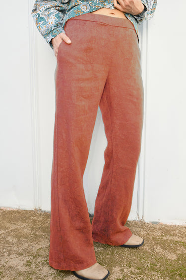 Person wearing a persimmon flared pants against a white wall.