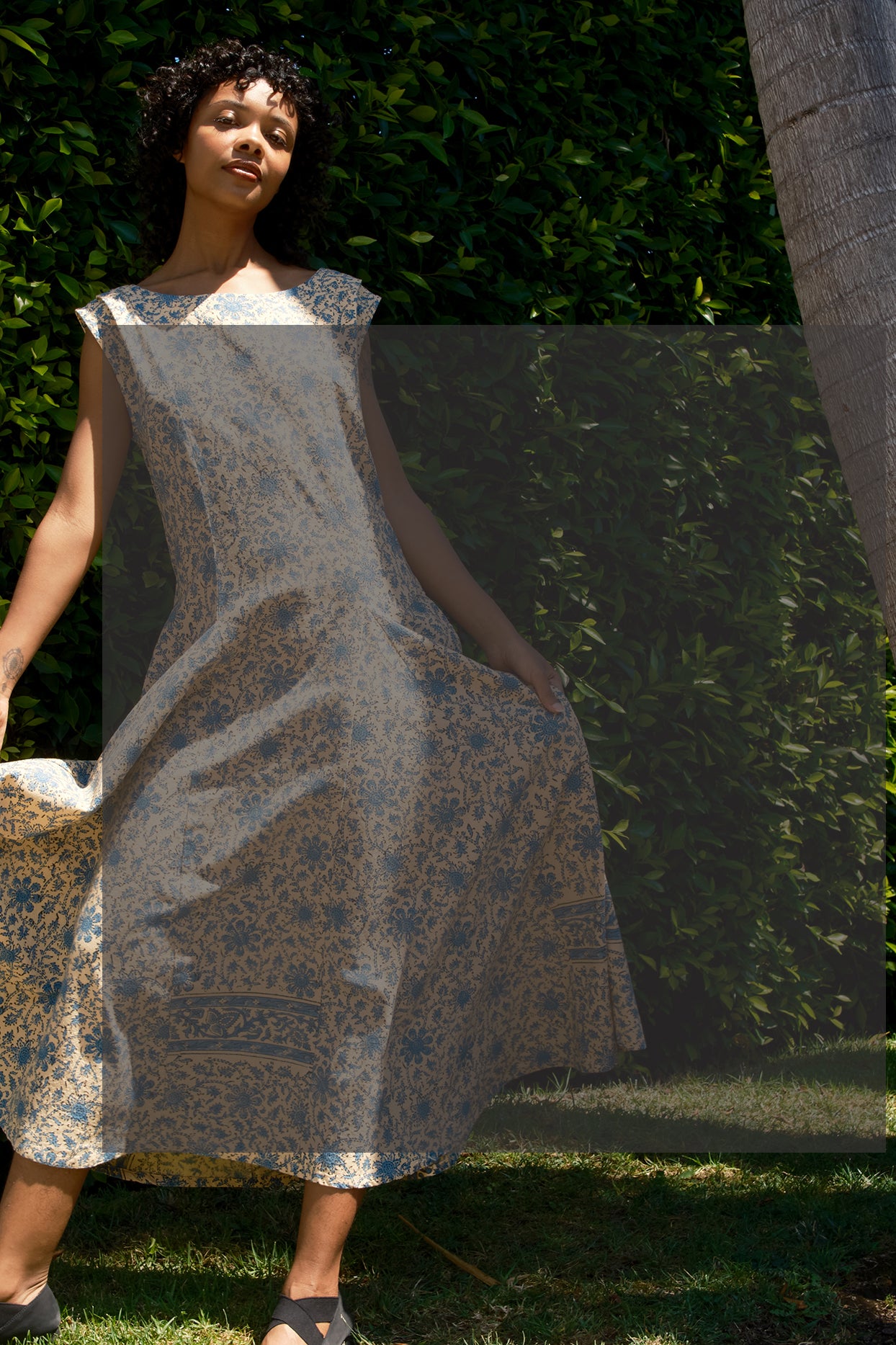 Woman wearing a patterned dress standing outdoors with greenery in the background