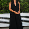 A woman wearing a black maxi caftan with deep cut arm holes and bias cut sides, featuring front cell phone pockets.