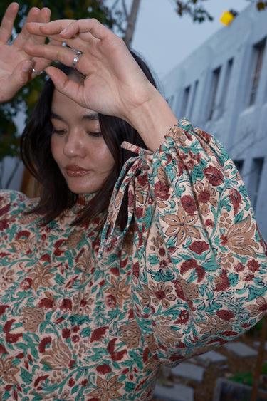Woman standing in garden wearing a long sleeve midi length dress in an ecru with red flower tapestry, showing sleeve detail.