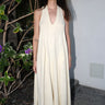 A woman outside wearing an alabaster off white maxi caftan with deep cut arm holes and bias cut sides, featuring front cell phone pockets.