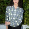 Woman outdoors wearing a gray with white and yellow ikat zip front jacket with black pants.