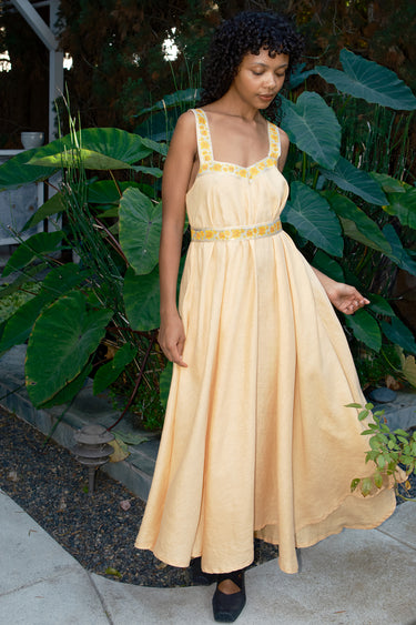 Woman in a long yellow dress standing outdoors with greenery around