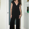 A woman standing in indoor setting wearing a slim black full length jumpsuit.