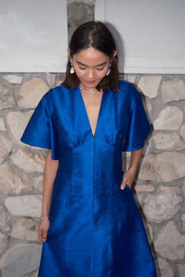 woman standing by stone wall wearing a sapphire blue zip front dress.