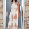 Woman standing in doorway wearing a white dress printed with warm brown trees.