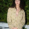A woman standing in front of greenery wearing a pea green calico tapestry baseball style jacket with a matching slip dress.