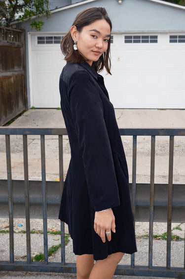 Woman standing outside wearing a black plush corduroy coat dress .