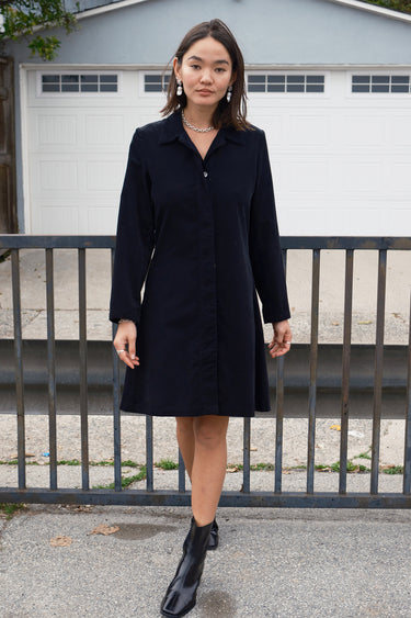 Woman standing outside wearing a black plush corduroy coat dress with black boots