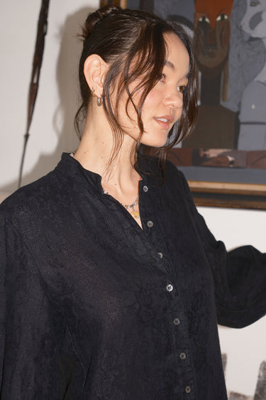 Person wearing a black button-up  coat in an indoor setting with a blurred background