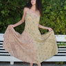 A woman wearing a mixed print slip dress of pea and blush calico tapestry, posing outdoors.