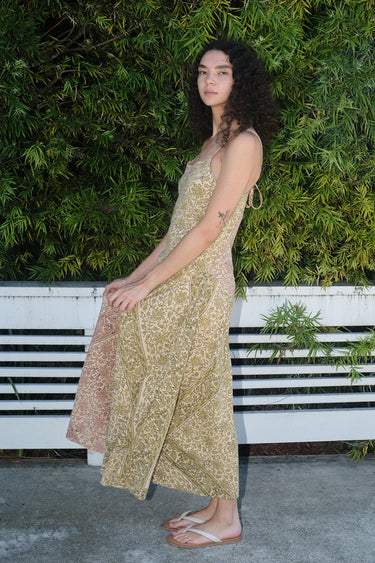 A woman wearing a mixed print slip dress of pea and blush calico tapestry, posing outdoors, side view.