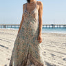 Woman in a floral dress standing on a beach with a pier in the background