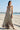 Woman in a floral dress standing on a beach with a pier in the background