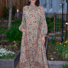 Woman standing in garden wearing a long sleeve midi length dress in an ecru with red flower tapestry.
