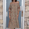 A woman standing in front of a door, wearing an off-the-shoulder floral tapestry dress with pockets, paired with boots.