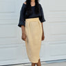 Woman wearing a black top and yellow skirt standing in front of a white garage door.