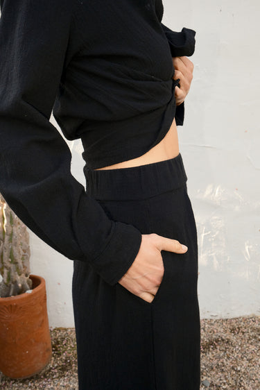 Person wearing a black outfit with a white wall and plant in the background