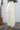 Person wearing a n alabaster  skirt standing next to a cactus plant against a white wall.