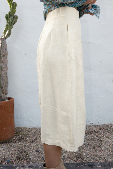 Person wearing a n alabaster  skirt standing next to a cactus plant against a white wall.
